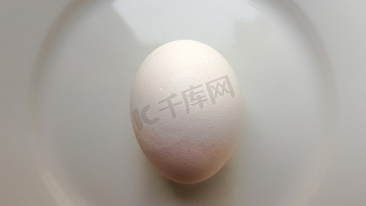 椭圆形的东西摄影照片_白盘子上的一个完整的生鸡蛋