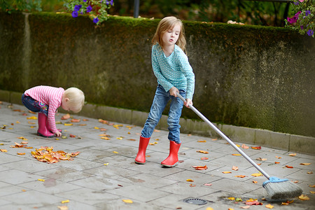 可爱的小女孩在秋天扫干树叶