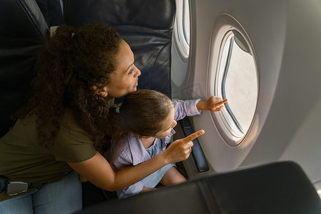快乐的母亲和她的女儿看着飞机窗外的风景