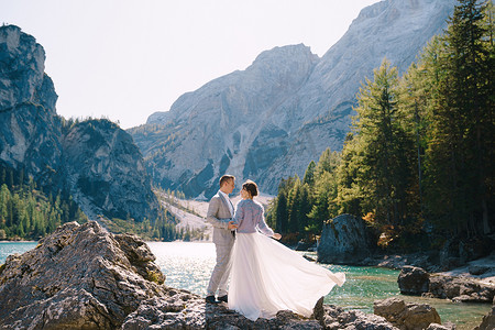 白云站摄影照片_新娘和新郎站在石头上俯瞰意大利的 Lago di Braies。