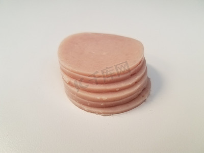 火腿肉切片摄影照片_白色表面上的一堆圆形粉红色火腿肉