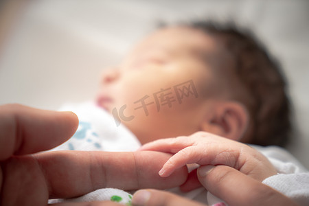 襁褓摄影照片_一个裹在襁褓中的新生女婴在安静地睡觉时，用她的小手和手指环绕着父亲和母亲的手指。