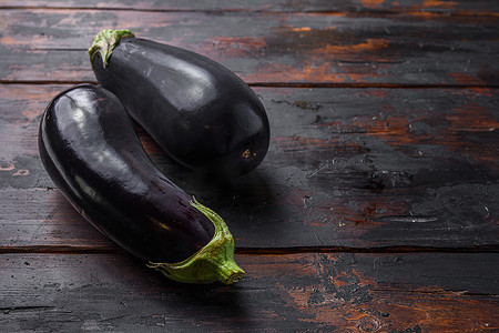 种茄子摄影照片_厨房旧深色木桌上新鲜健康的生紫色茄子。
