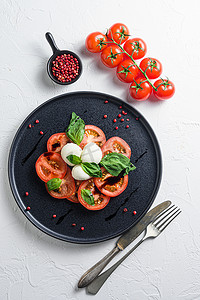 Caprese 新鲜意大利沙拉配西红柿、马苏里拉奶酪、深色石板上的绿色罗勒，白色背景顶视图选择性聚焦垂直