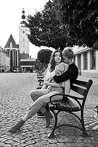 美丽的年轻夫妇拥抱在欧洲小镇的长凳上。 