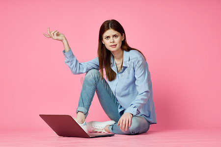 购物娱乐摄影照片_女人坐在地板上，笔记本电脑购物娱乐粉红色背景