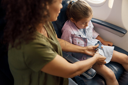 母亲帮助她的小女儿在飞机上调整并系紧安全带以确保飞行安全
