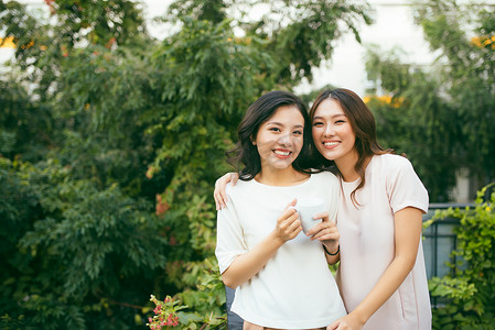 外边摄影照片_两位穿着考究的漂亮年轻女性在户外边喝咖啡边聊天