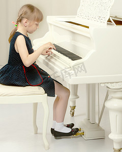 美丽的小女孩正在一架白色的三角钢琴上弹奏。