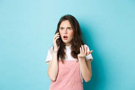 站在蓝色背景下，困惑而震惊的女性在用智能手机聊天时收到坏消息，接到不好的电话