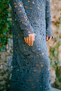 穿着时尚蓝色蕾丝连衣裙的女人的手站着，墙壁上缠绕着常春藤，特写