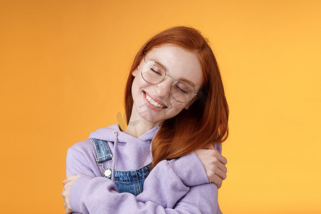 感恩心摄影照片_特写浪漫可爱迷人的红发女孩享受温暖爱歪头闭眼梦幻成像完美约会拥抱自己拥抱自己的身体接受身体积极性橙色背景