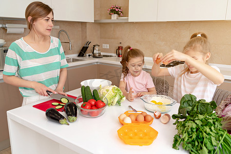 面粉做饭摄影照片_母亲和两个女儿在厨房做饭，享受快乐、幸福的家庭和单身母亲的概念