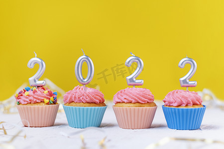 黄色背景中以数字 2022 形式出现的节日纸杯蛋糕和蜡烛。