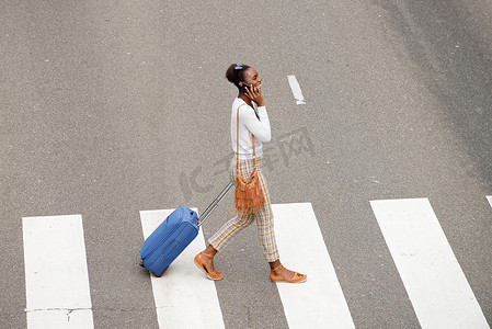 非洲裔美国妇女带着旅行袋和手机过马路的侧面肖像