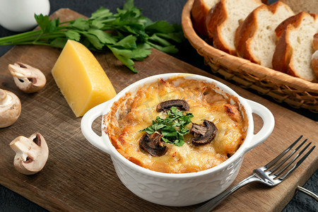 砂锅配鸡肉、蘑菇和奶酪，在俄罗斯被称为白碗里的朱丽叶，木板上放着香草，特写