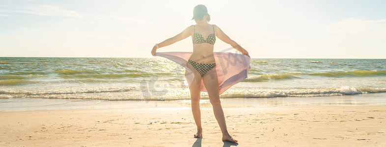 女人拿着毛巾站在沙滩上，背景是大海
