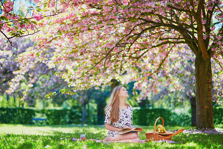 公园野餐摄影照片_美丽的年轻女子在盛开的春天公园野餐