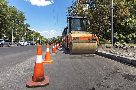 橙色路锥保护城市街道边缘的重型轮式压实机