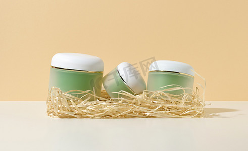 带白色盖子的空化妆品绿色罐子躺在白色桌子上的木屑中，米色背景。