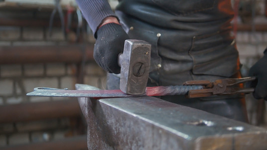肌肉男铁匠用锤子在锻造中制造钢刀