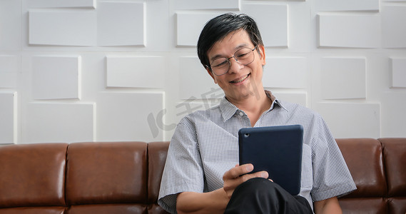 亚洲老人在客厅的沙发上玩平板电脑和视频通话