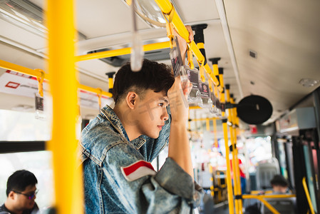 穿着休闲西装的亚洲男乘客，站在公共汽车内。