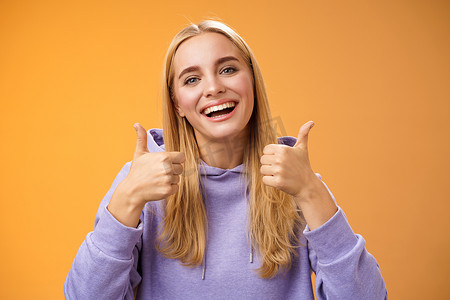 x展架产品推荐摄影照片_特写迷人、高兴、可爱的女性顾客给予积极反馈，竖起大拇指，像微笑的手势，广泛同意推荐完美的产品护肤站立满意的橙色背景