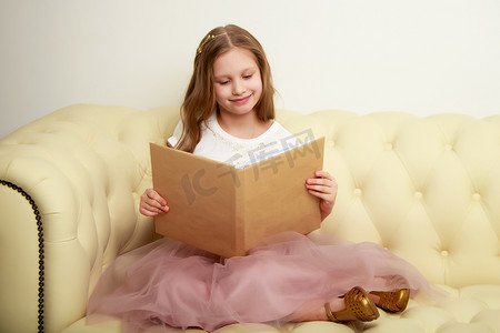 一个小女孩坐在沙发上看书。
