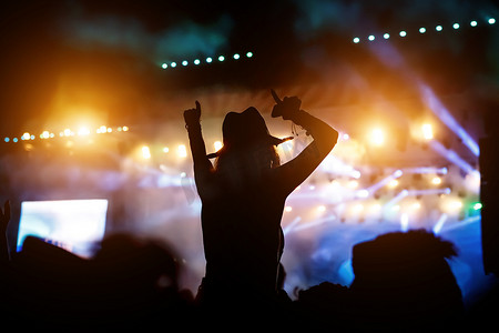 歌手剪影摄影照片_一个女孩在群众活动中举手的剪影。