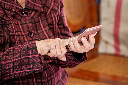 亚洲老妇人坐着看现代智能手机上的东西，与家里的其他人建立联系，生活技术，特写