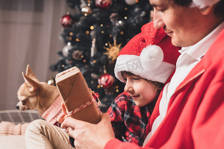 幸福的家庭在圣诞老人的帽子，父亲和孩子的儿子在家里送圣诞礼物。