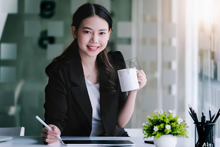 女性营销经理在使用平板电脑和营销分析论文之前，一边工作一边喝咖啡以减少睡意。