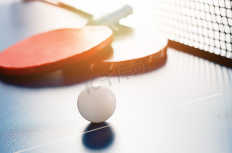 乒乓球招新摄影照片_网附近的乒乓球桌上放着两个网球拍和一个白球。