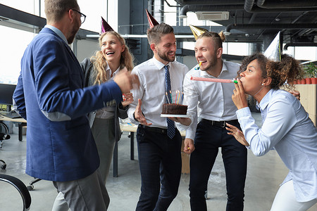 快乐的商业团队带着生日蛋糕在办公室聚会上向同事致意