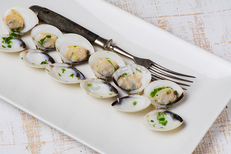 白葡萄酒中的蛤蜊和欧芹放在质朴的长方形盘子里