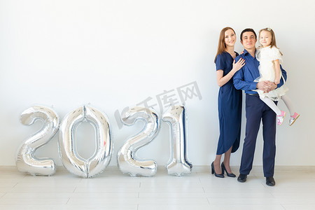 年轻幸福的家庭母亲、父亲和女儿站在白色背景上形状像数字 2021 的气球旁边。