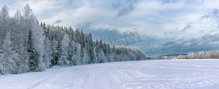 冬季森林、冰冻河流和上方厚厚的深蓝色雪云的全景。