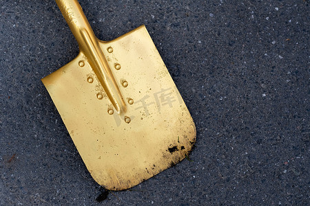 金铲摄影照片_一把金色的铲子躺在柏油路上。开幕式