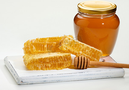 白色木板上装有蜂蜜的玻璃透明罐和蜂蜜蜡蜂窝片