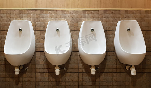 小便器摄影照片_四个小便池排列在现代男式公厕的瓷砖墙上，毫无隐私可言。