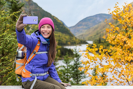 快乐的亚洲徒步旅行者女人在户外自然秋山景观的风景点上用智能手机自拍。