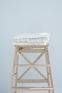 一堆干净的浴巾彩色棉毛圈纺织品堆放在木椅上，靠近白墙堆概念特写