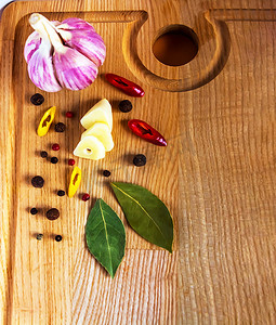瓣叶摄影照片_整个头和一瓣大蒜，切成薄片，红辣椒和黄辣椒，切成环，月桂叶和豌豆的混合物放在木砧板上。