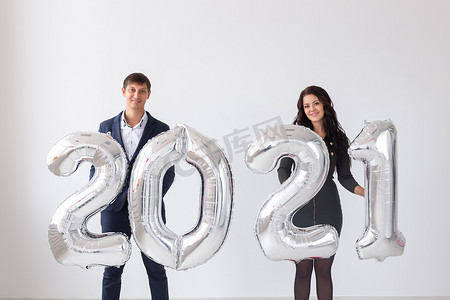 新年、庆典和假期概念 — 一对情侣在白色背景下用银气球制成的2021标志玩得开心