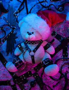 游戏皮肤摄影照片_戴着圣诞老人帽子的玩具熊是霓虹灯下 BDSM 游戏的圣诞礼物