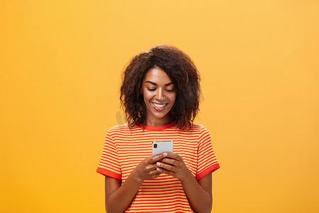 手机小应用摄影照片_通过智能手机消息应用程序输入对派对邀请的回答，将设备放在胸前，对着小工具屏幕开心地微笑，发短信或玩有趣的游戏，在地铁上的橙色墙壁上浪费时间