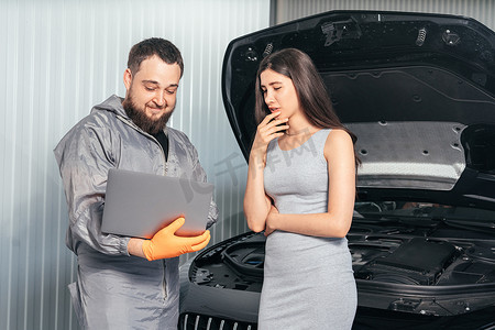 汽车修理工在使用笔记本电脑时与女性顾客交流，并在汽车维修店检查车辆故障
