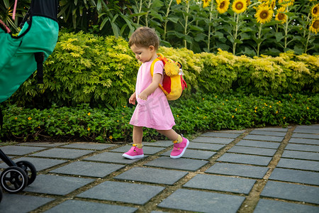穿着粉红色连衣裙、背着婴儿背包的可爱女婴在公园的路上走