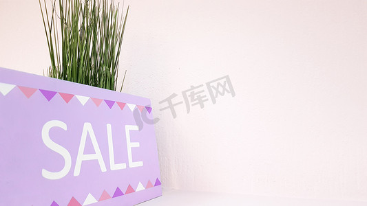 在一家女装店的浅粉色墙壁和绿色植物的背景上，在架子上签上折扣铭文。